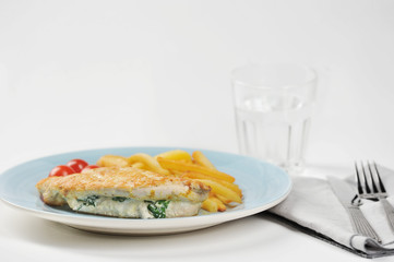 On the plate is a chicken breast stuffed with spinach and ricotta. Next to the plate is a glass of water, a napkin and cutlery. Light background. Close-up.