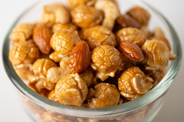 Caramel popcorn with cashew nuts and almonds in a white background, selective focus.