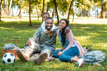 Happy African American soldier sitting on grass with family in park