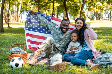 Happy African American soldier in military uniform and family holding American flag in park