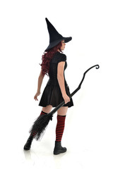 full length portrait of red haired girl wearing black witch costume and pointy hat, holding a...