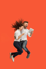 Image of young couple over red background using laptop computer or tablet gadget while jumping.