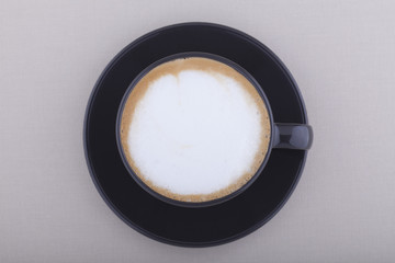 Black cup of cappuccino with foam on textile background