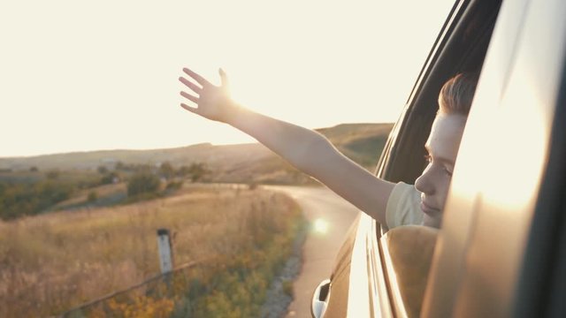 Teen Boy Looking Out The Car Window And Waving His Hand.