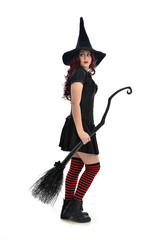 full length portrait of red haired girl wearing black witch costume and pointy hat, holding a broom. standing pose, isolated on white studio background.