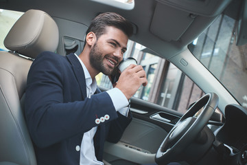 Young attractive businessman in car drink coffee and talking on the phone