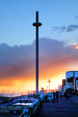Brighton promenade at sunset with the moving viewing tower in the centre the promenade is very busy a pride flag is flying in the background the sky is orange and red from the setting sun