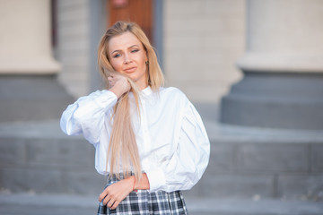 portrait of a blonde on a building background with columns. beautiful blonde in a white blouse smiling