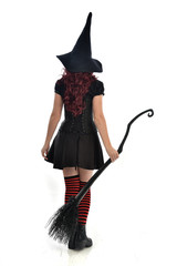 full length portrait of red haired girl wearing black witch costume and pointy hat, holding a...