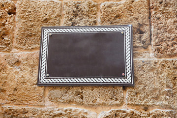 A brown sign with a white frame hangs on a stone wall.
