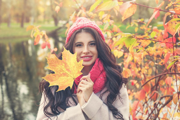 Autumn woman with bright maple leaf outdoors. Beautiful brunette girl in fall park