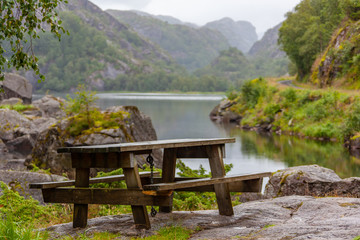 Brown wooden table and benches on the stone in the picnic area near lake in the mountain valley at murky day in Rogaland country, Norway