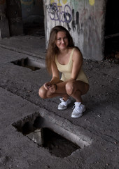 Sexy young woman in swimsuit is squatting next to the hole in the floor in abandoned building