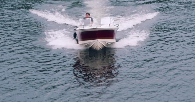 Drone shot of millennial man accelerating  outboard motor boat on northern lake