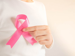 Breast Cancer Awareness Month in October. Closeup of woman in white shirt showing satin pink ribbon awareness for support people who live w/ breast cancer. Health care and medical concept. Copy space.