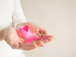 Breast cancer awareness campaign in October. Closeup of female hands holding satin pink ribbon...