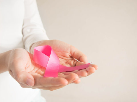 Breast cancer awareness campaign in October. Closeup of female hands holding satin pink ribbon symbolic for support breast cancer/tumor patients. Women's health care and medical concept. Copy space.