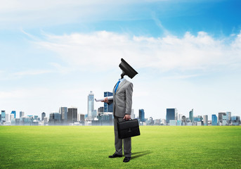 Camera headed man standing on green grass against modern cityscape