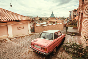 Old street of georgian capital with traditional houses and small retro car ZAZ Zaporozhets.