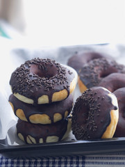 Stacked up doughnuts coated with chocolate and sprinkles on top on a tray lined with parchment paper, fresh out from oven