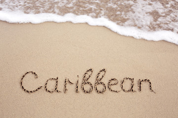 Word Caribbean written on the sand near the sea.
