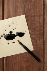 An overhead photo of drops of ink on paper and a nib pen, with place for text