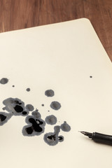 A photo of drops of ink on paper and a nib pen, with place for text