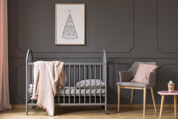 Poster above kid's bed with blanket next to grey armchair with pink pillow in bedroom interior....