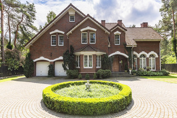 Front view of a red brick English style classic house with a steep roof, large windows and a...
