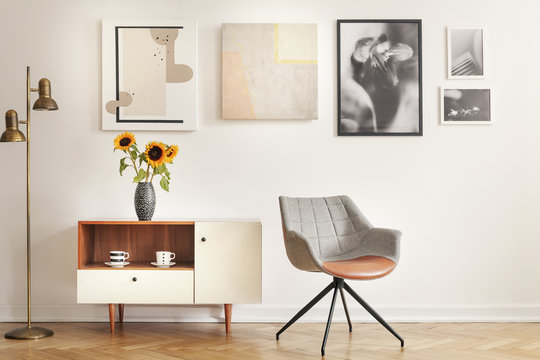Grey armchair next to cupboard with sunflowers in white room interior with gallery. Real photo