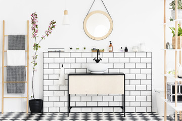 Real photo of a bathroom interior with a cupboard, tiles, mirror, flower and ladder with towels