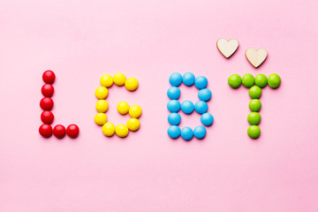sweet colorful candies organized as word LGBT and two handmade wooden hearts on pink background