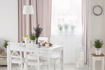 Real photo of white table with fresh lavender and breakfast standing in bright dining room interior with window with drapes