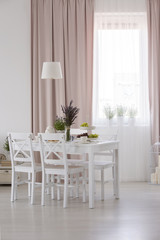Real photo of white dining room interior with window with curtains, table with fresh lavender and food and lamp