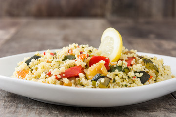 Couscous with vegetables in plate on wooden table