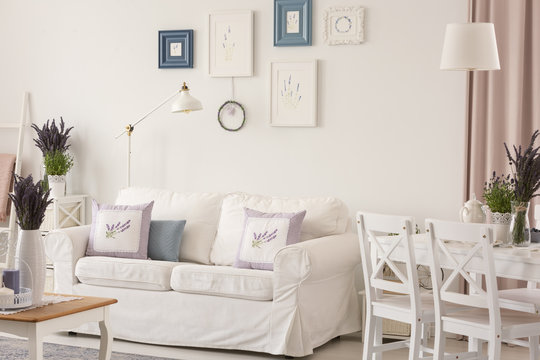 White room interior with couch with pillows, posters on wall, dining table with chairs and fresh lavender in the real photo