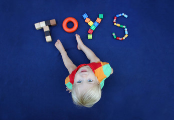 Little blond boy with inscription TOYS made from different toys on blue textile background. Childhood concept. Good for baby store