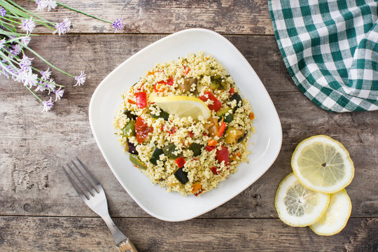 Couscous with vegetables in plate on wooden table. Top view