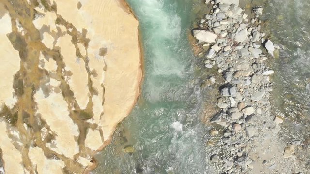 Aerial: flight over river flowing between eroded rocks and gravel. Native Cinelike D-Log ungraded flat color profile.