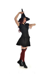 full length portrait of red haired girl wearing black witch costume and pointy hat.  standing pose, isolated on white studio background.
