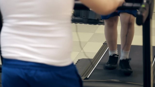legs and thick body of little overweighted boy who trains on treadmill in gym