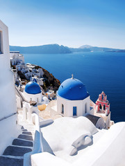 View with Greek orthodox church with blue domes and sea in Oia in Santorini, Greece, Europe. Beautiful scenery above the caldera overlooking the Aegean Sea.
