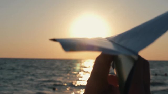 Silhouette of a boy playing with a paper airplane on a sea beach at sunset