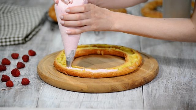 Half of a Paris Brest cake. Background: a pastry bag filling with whipped cream.