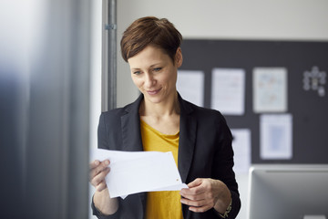 Attractive businesswoman standing in office, reading document