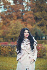 Attractive woman fashion model brunette in coat on autumn park background