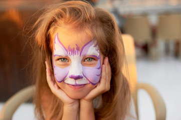 Pretty exciting blue-eyed girl of 5 years with a pink face painting