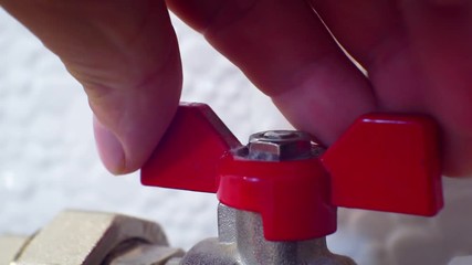 red valve on the pipe is closed by a male hand.close-up