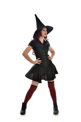 full length portrait of red haired girl wearing black witch costume and pointy hat.  standing pose, isolated on white studio background.