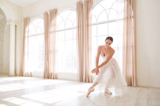 Ballerina dancing in a studio on white background window.